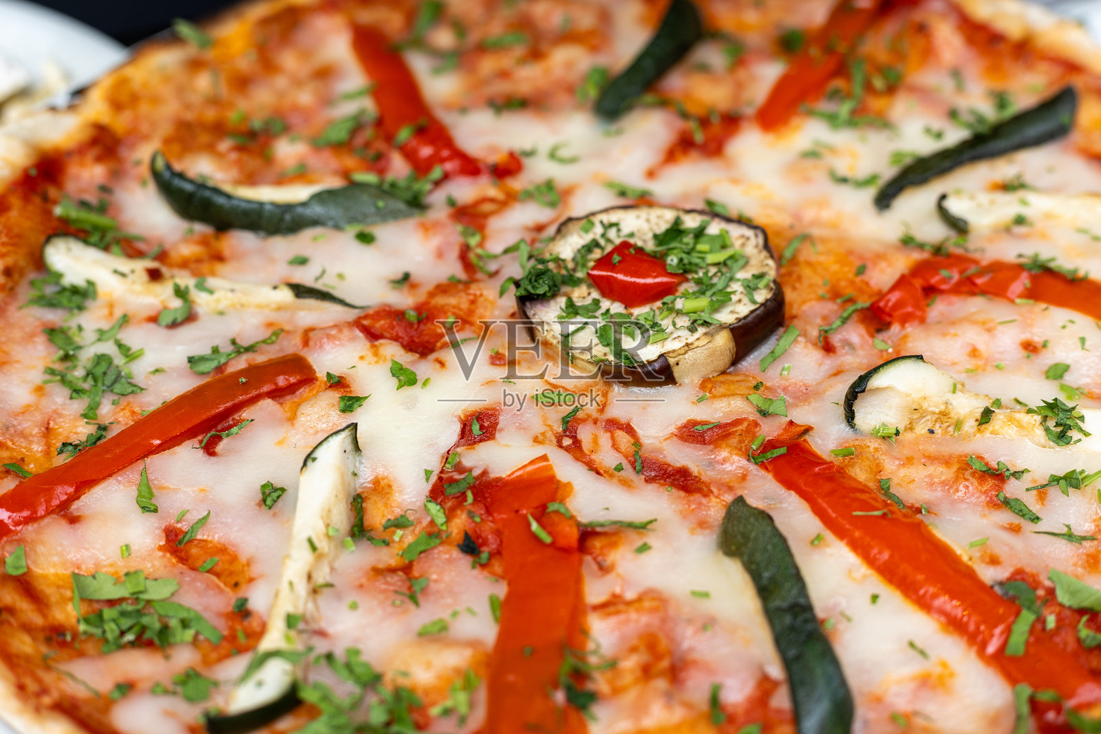 新鲜出炉的蔬菜披萨，上面撒有香草、辣椒和奶酪，摆放在一家温馨的餐厅里。照片摄影图片