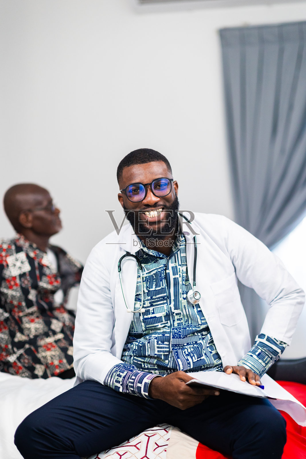 一位成功的年轻非洲医生与他身后的老年患者的肖像。家庭医疗访问。照片摄影图片