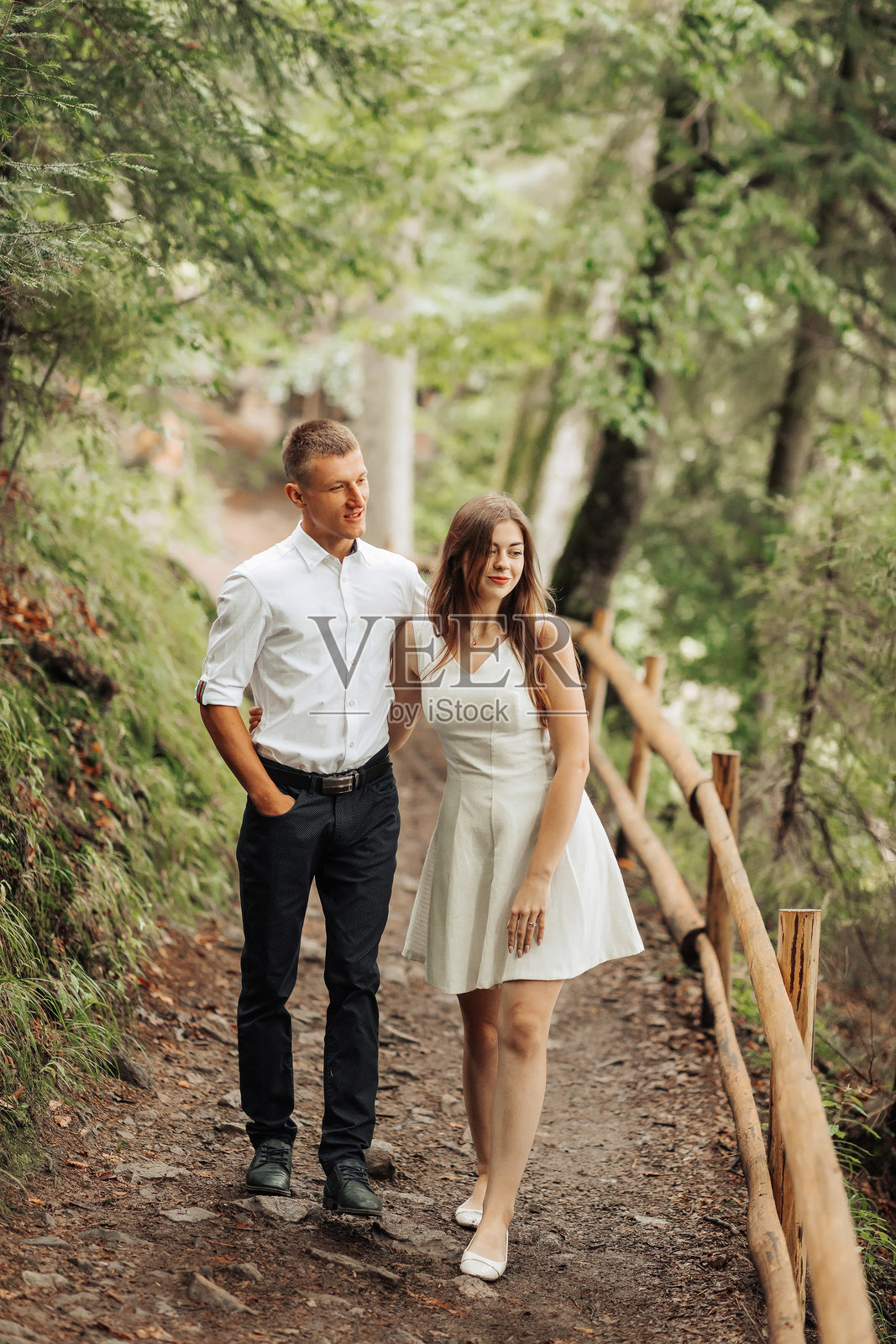 一对情侣在树林的小路上散步，男士穿着白色衬衫。照片摄影图片