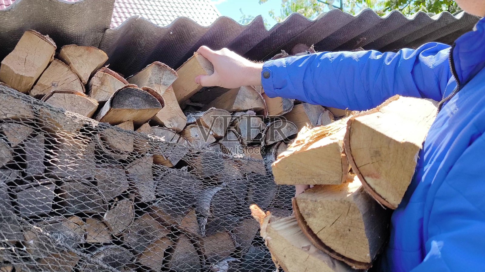 一个男人从院子里的木柴堆中取木柴。照片摄影图片