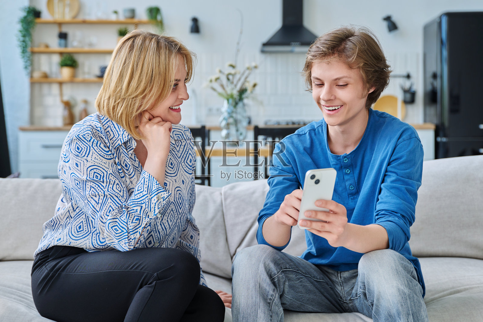 中年母亲和青少年儿子坐在家中一起看智能手机照片摄影图片
