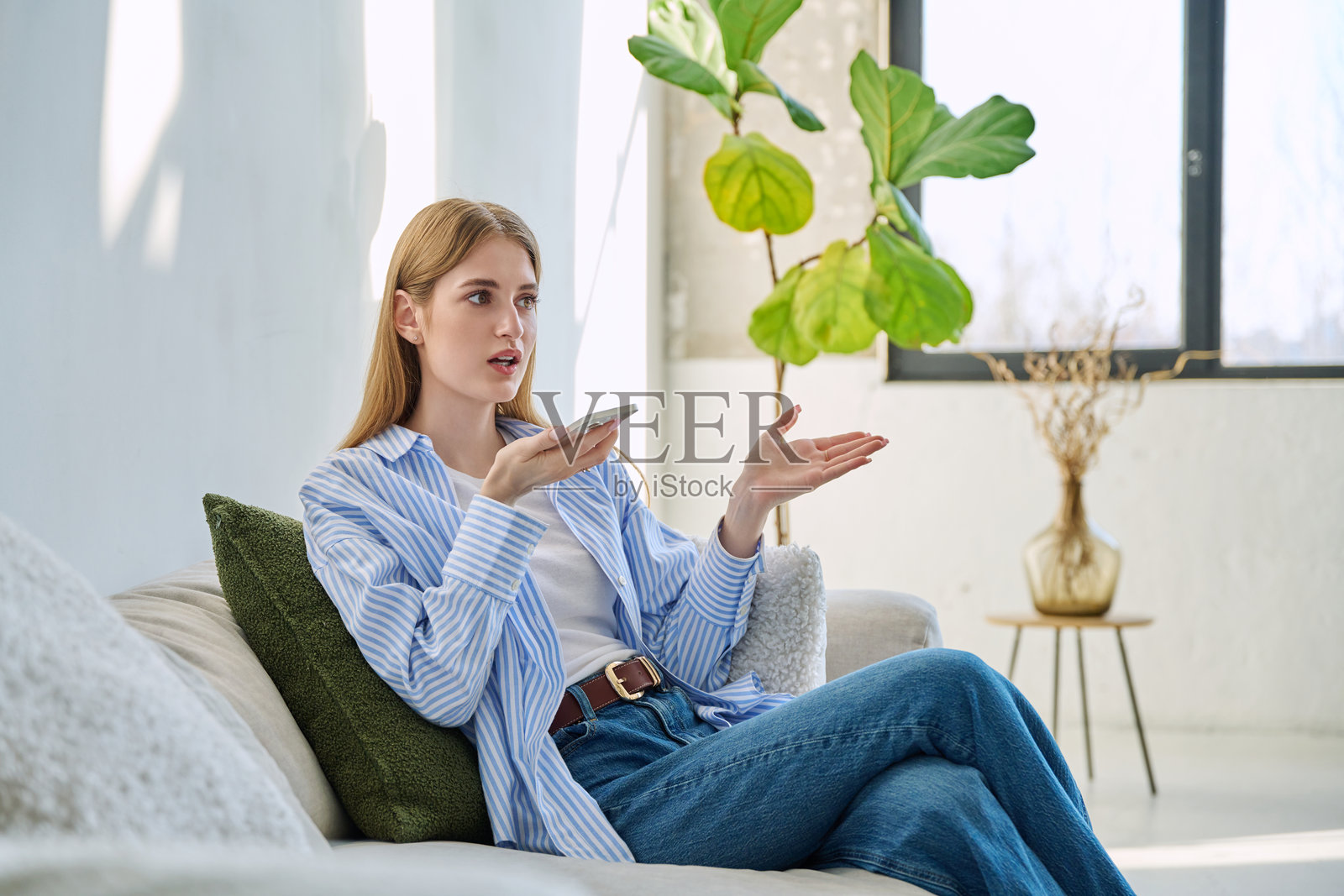 年轻女性坐在家里的沙发上使用智能手机录制语音信息照片摄影图片