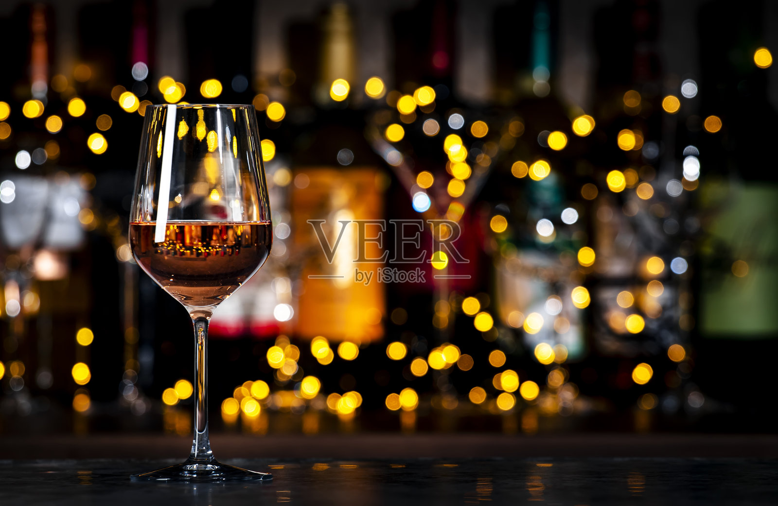 深色酒吧背景下，带有散景灯光的酒杯和酒瓶中的法式粉红葡萄酒安茹玫瑰。照片摄影图片