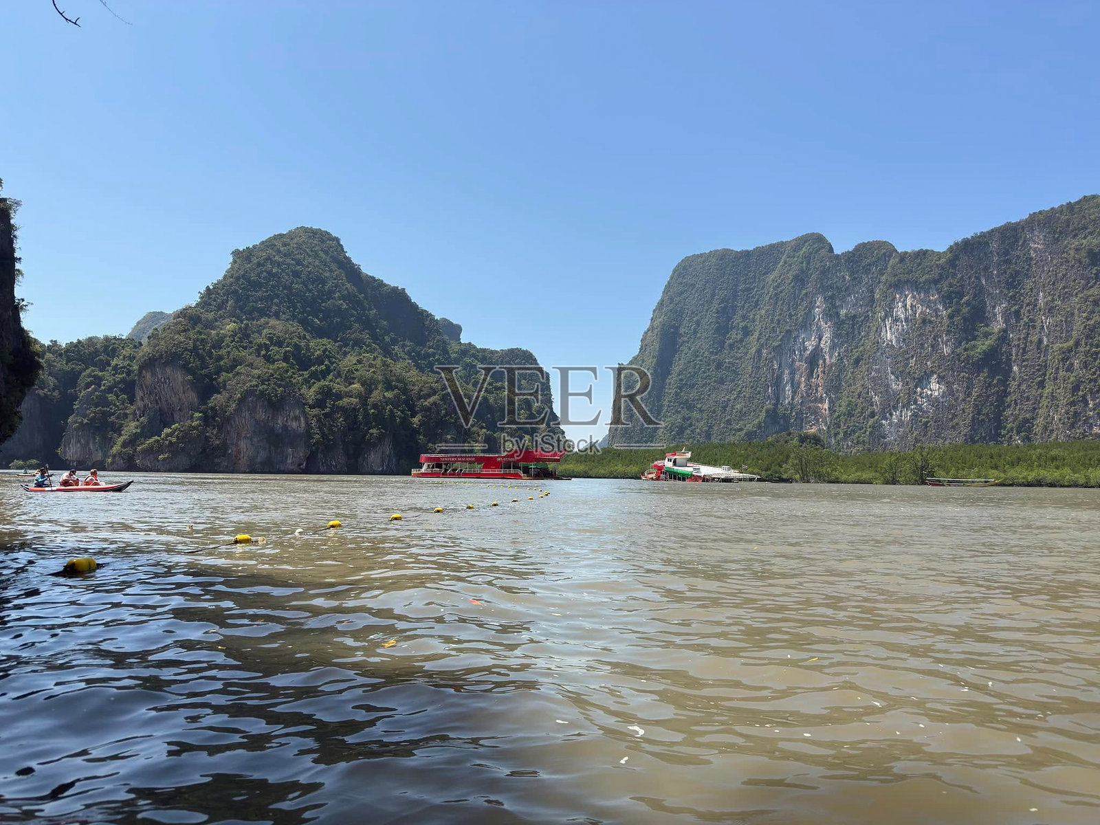 壮丽的石灰岩悬崖环抱着宁静的水域，映衬在明亮的蓝天之下，这幅宁静的海湾风景展现了自然之美与冒险精神。照片摄影图片