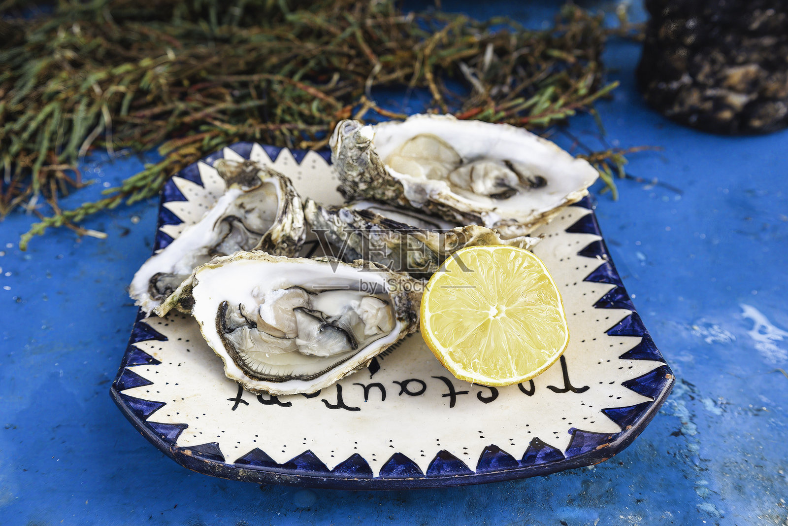 新鲜生蚝配柠檬，放在传统摩洛哥陶瓷盘上，蓝色桌子，来自摩洛哥埃索伊拉港的海岸美食照片摄影图片