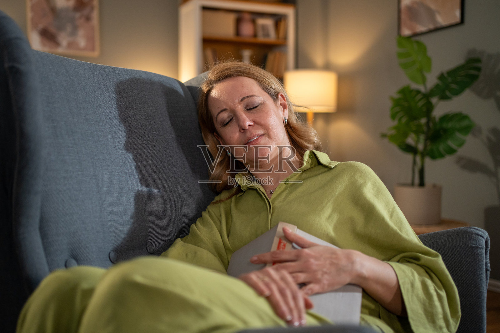 安静的女人在扶手椅上打盹，手中拿着一本书：在家中寻找宁静照片摄影图片