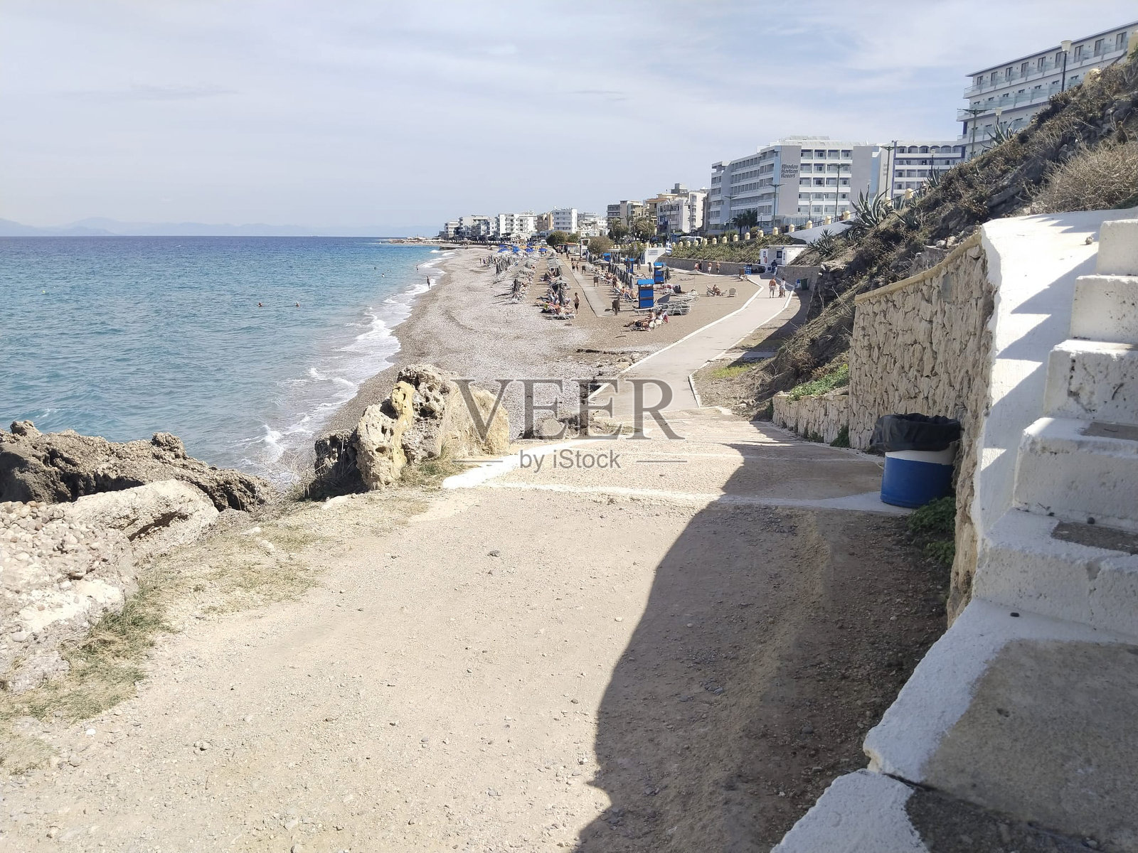 温柔的海浪轻轻拍打着阳光照耀的海岸，人们在海滨小镇的沙滩上漫步。照片摄影图片