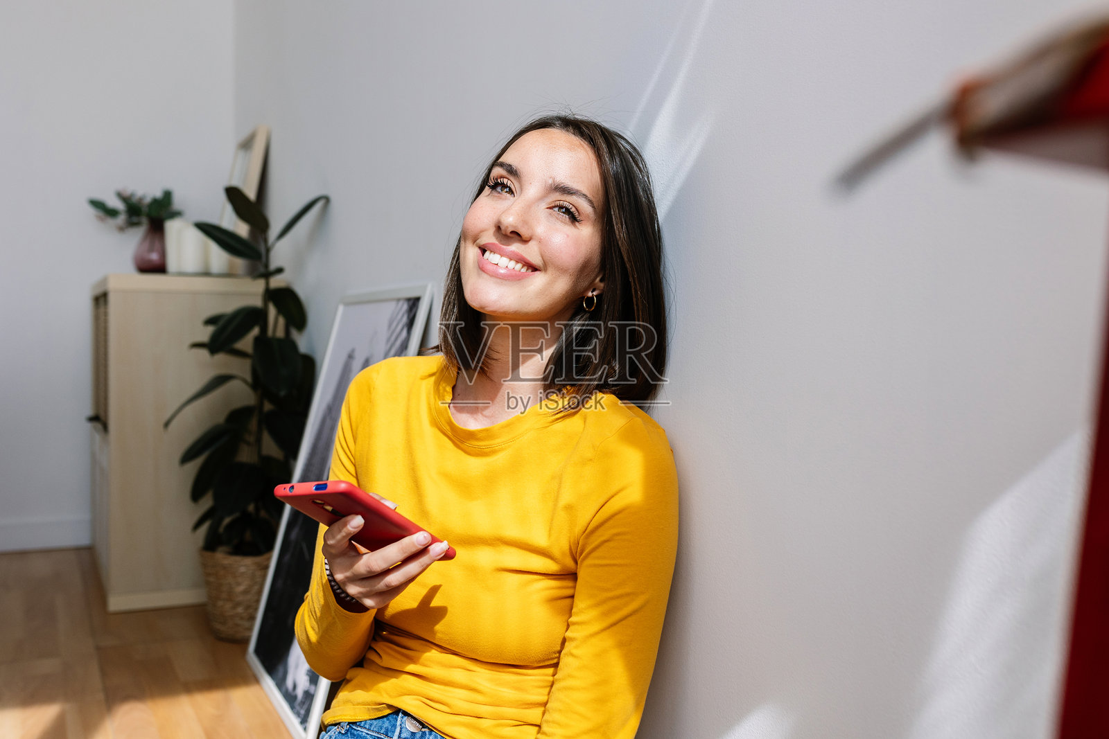 微笑的年轻美女在家中放松，手里拿着手机照片摄影图片