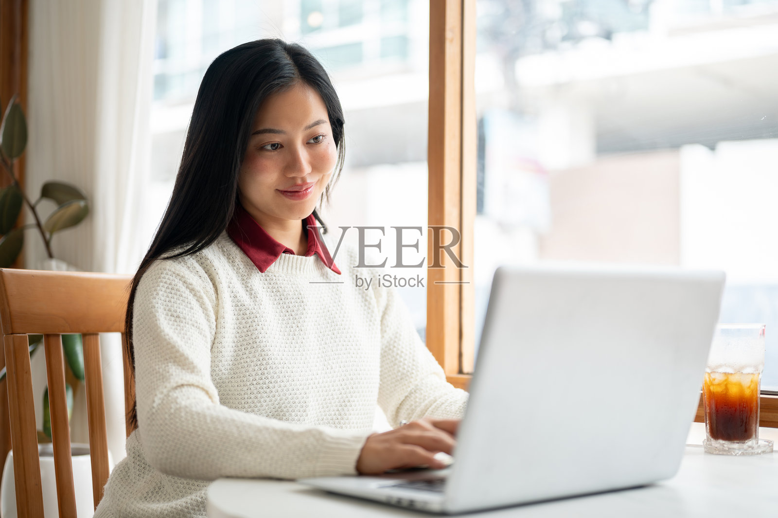 一位微笑的亚洲女性正在打字，专注地看着笔记本电脑屏幕。在咖啡馆工作或学习。照片摄影图片