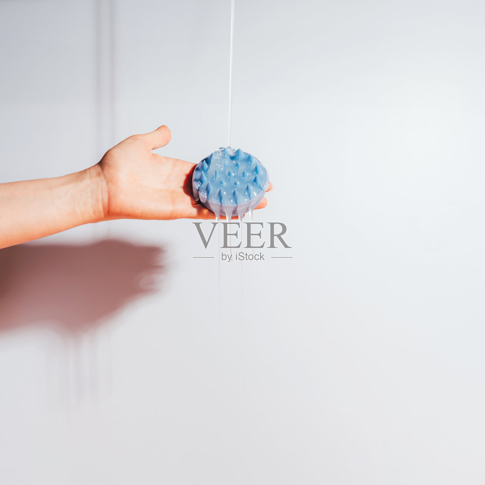 手握蓝色头皮按摩器，洗发水流淌其上照片摄影图片