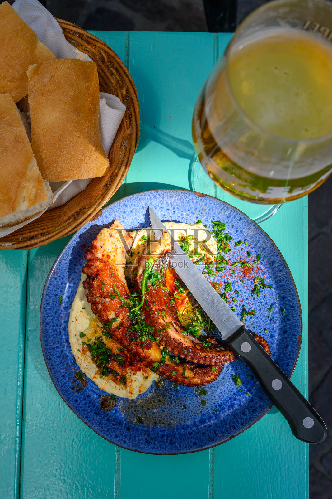 温暖的阳光照耀着安特卫普大广场户外绿色桌子上的烤章鱼盘。照片摄影图片