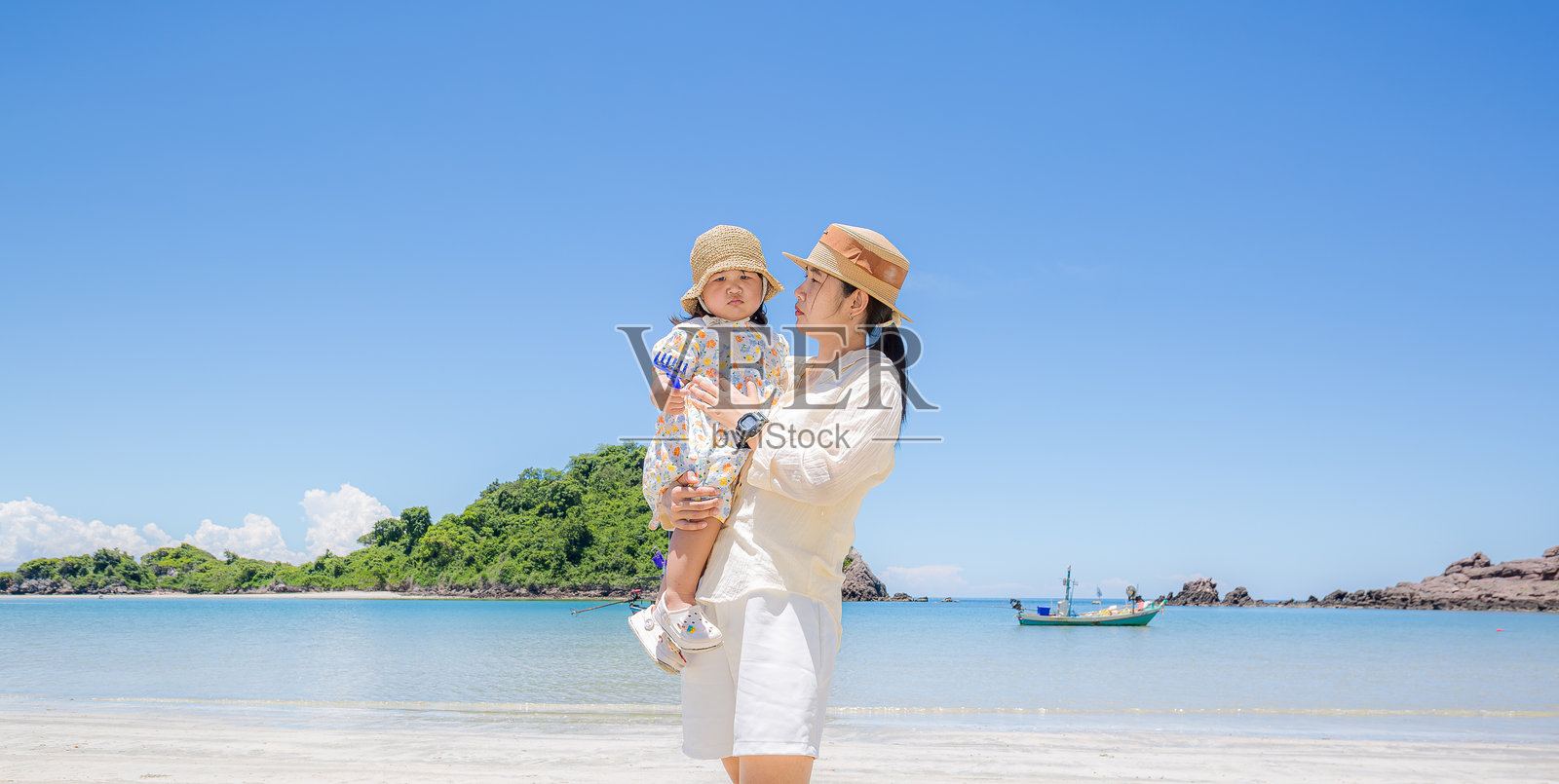 母亲在海边的沙滩上抱着女儿，度假时美丽的海滩。快乐的亚洲家庭在海滩度假。母亲和小女儿在热带海滩上一起散步和玩耍，享受夏季日落。照片摄影图片