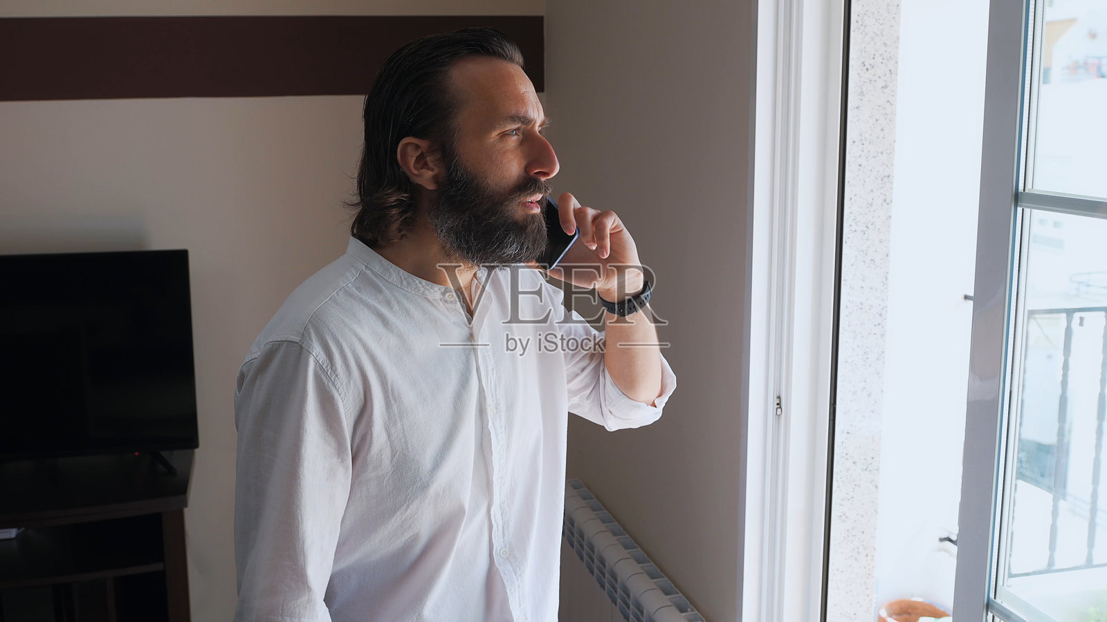 自信的胡子男人在窗边用智能手机通话照片摄影图片