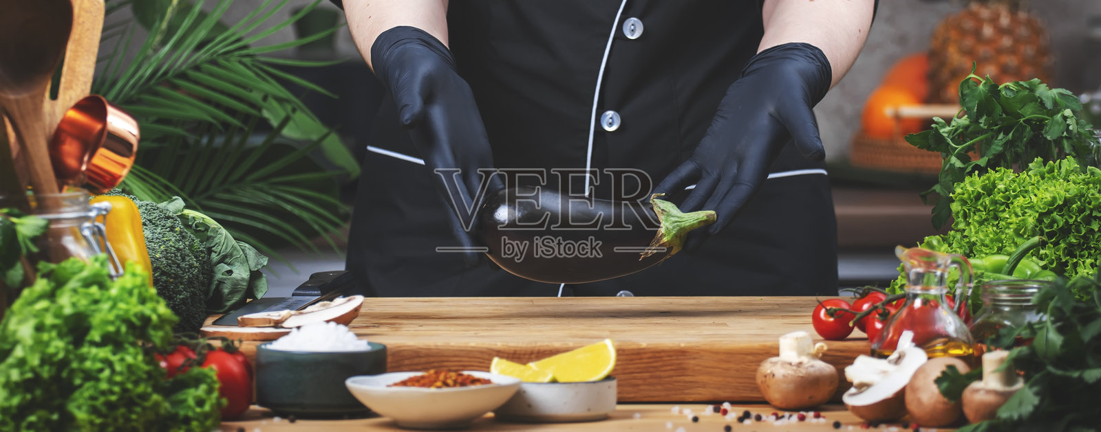 在厨房烹饪食物。厨师手中拿着新鲜的茄子。木桌、厨房用具、蔬菜、香草和配料。健康的素食饮食、食谱、博客。照片摄影图片
