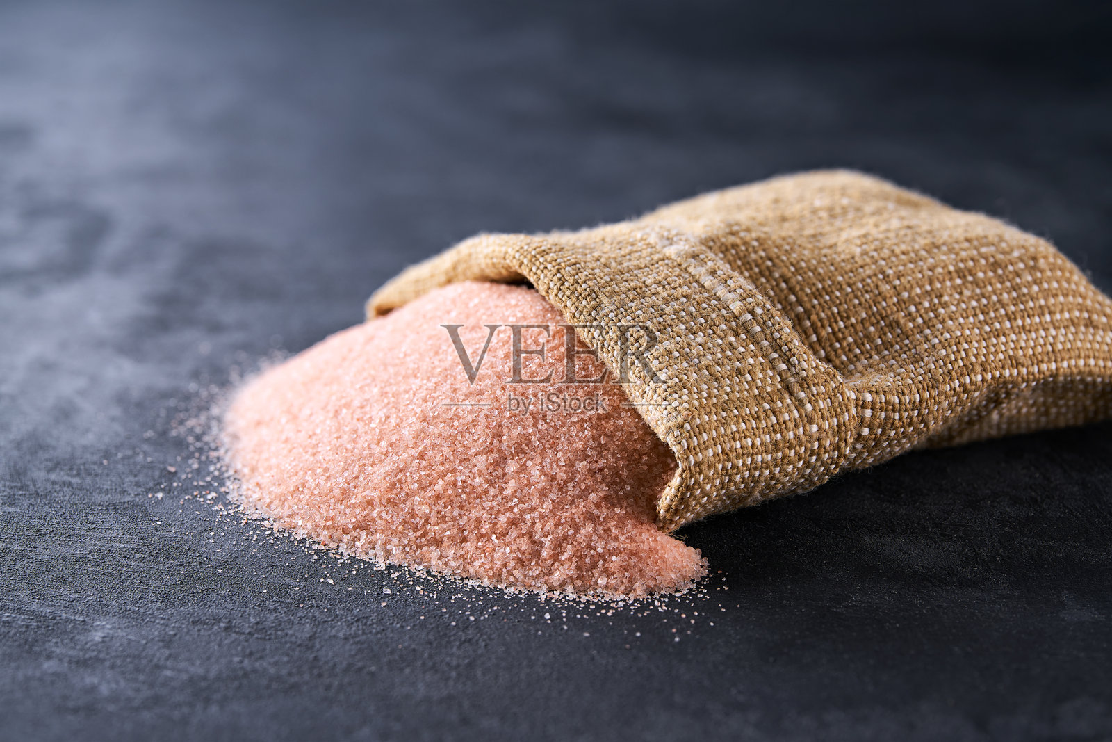 喜马拉雅盐从袋子里洒落在黑色桌子上，选择性对焦。照片摄影图片