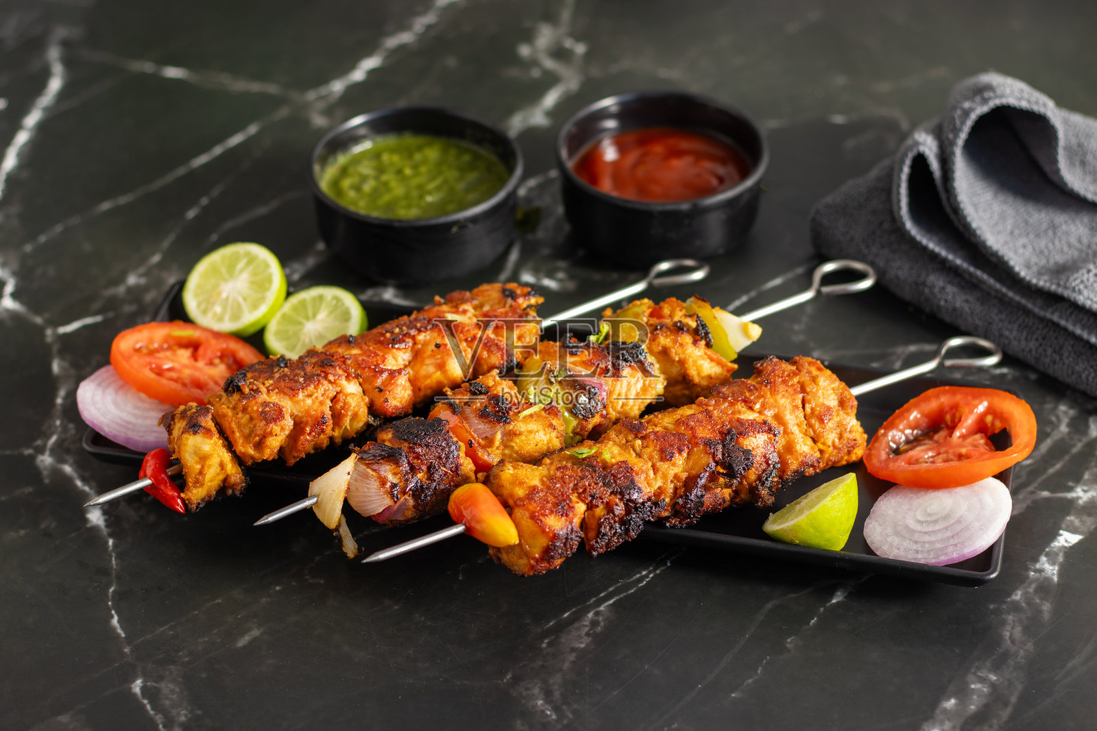 铁板烤鸡肉串或鸡肉提卡烤肉串，配有蔬菜，旁边有切片番茄、洋葱、青柠和蘸酱。照片摄影图片