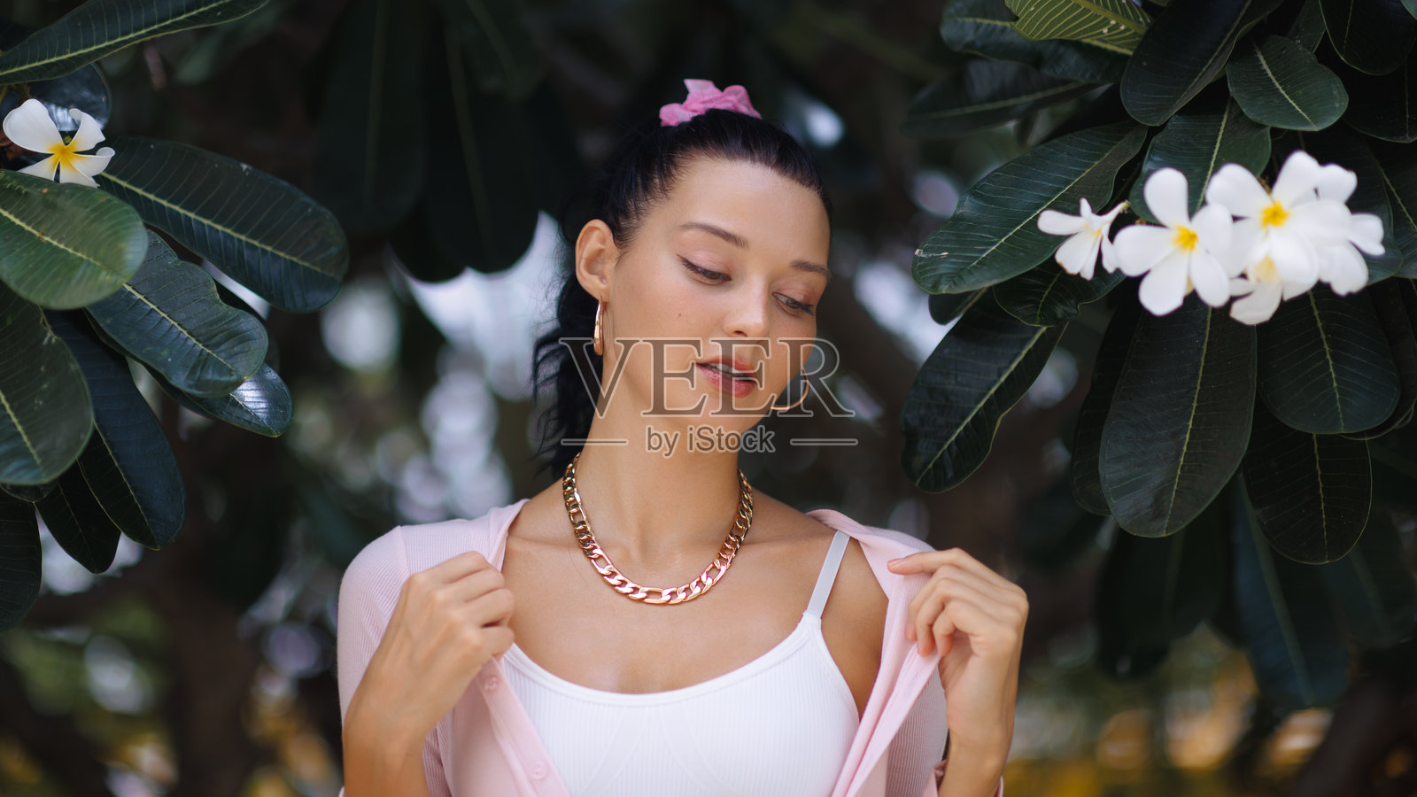 穿着粉色开衫的时尚女性在热带花卉下户外摆姿势照片摄影图片
