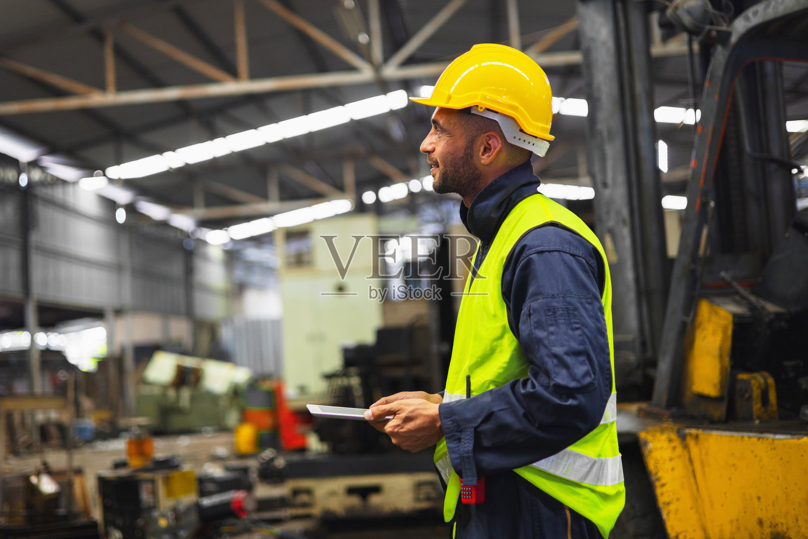 戴着黄色头盔和安全背心的男子站在工厂里照片摄影图片