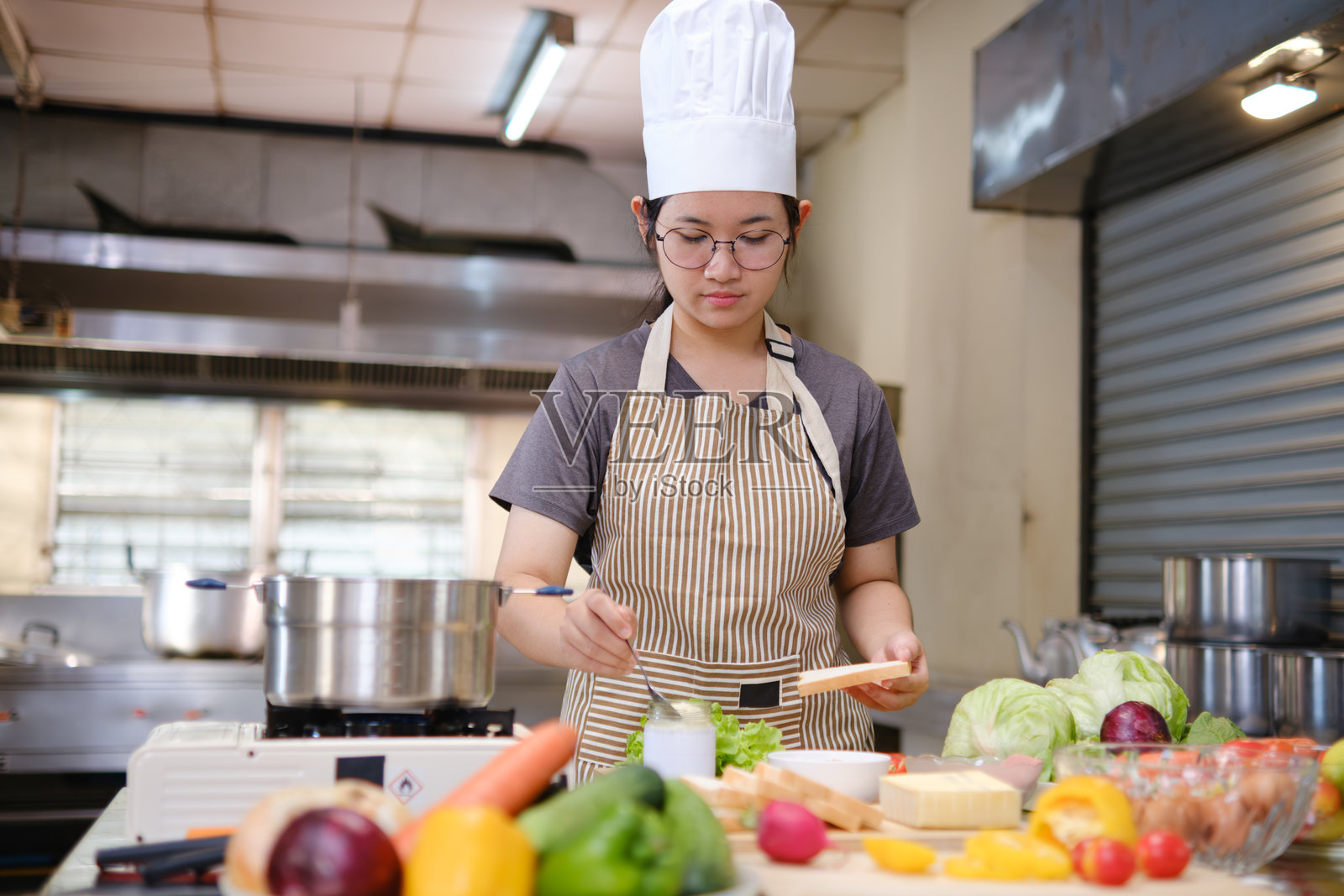 专注的厨师在专业厨房中仔细制作美味三明治，周围新鲜食材一览无余照片摄影图片