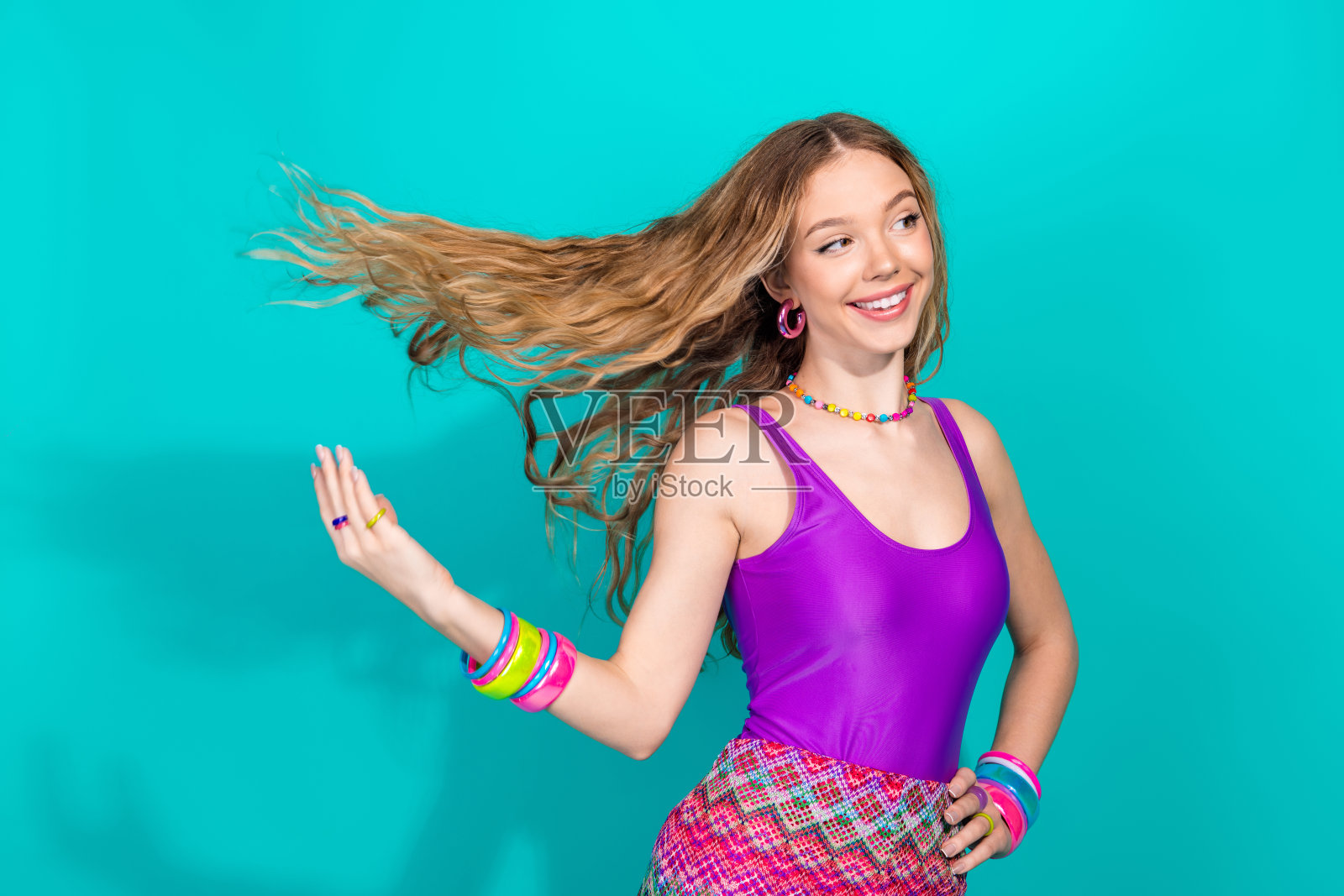 充满活力的年轻女性，穿着时尚复古服装，背景为青绿色，展现出快乐和魅力，摆出轻松俏皮的姿势。照片摄影图片