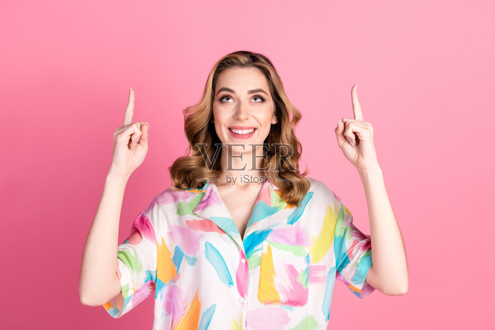 微笑的年轻女性穿着色彩斑斓的衬衫，在粉色背景前热情地做手势，象征着快乐和积极。照片摄影图片