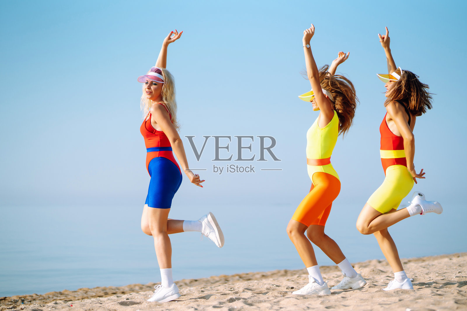 三位年轻女性穿着色彩缤纷的服装，在日出海滩上尽情玩乐。照片摄影图片