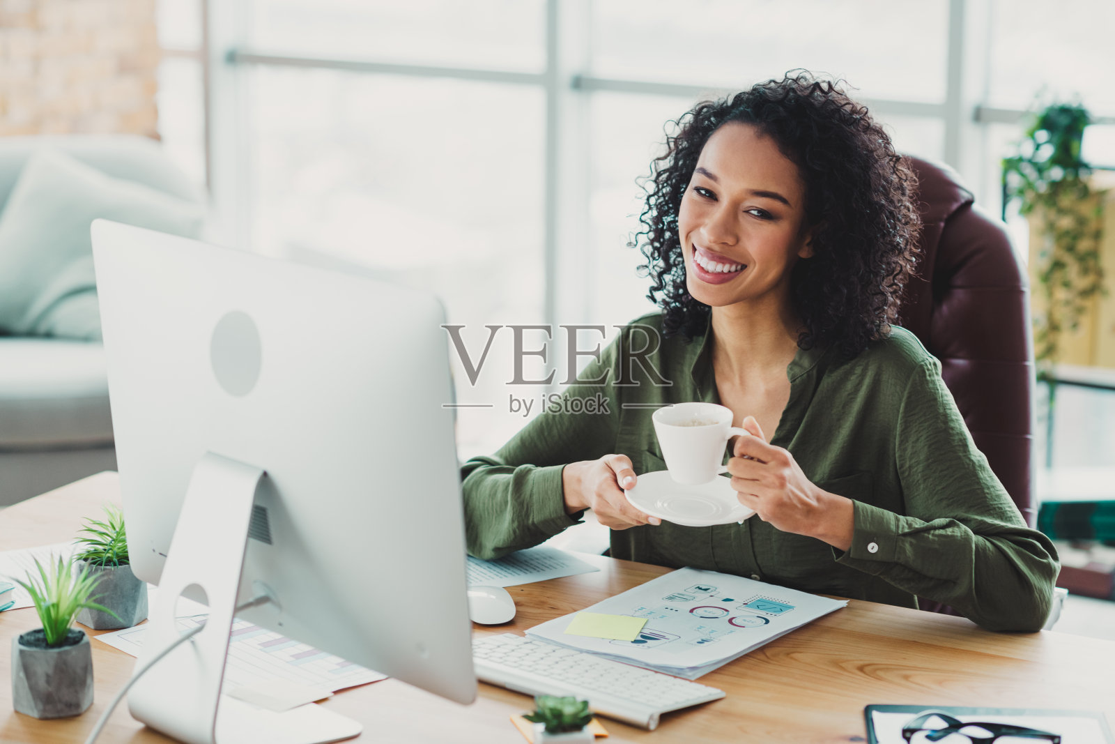 年轻女商人在明亮现代的办公室工作空间中享受咖啡，同时在电脑上处理商业报告。照片摄影图片