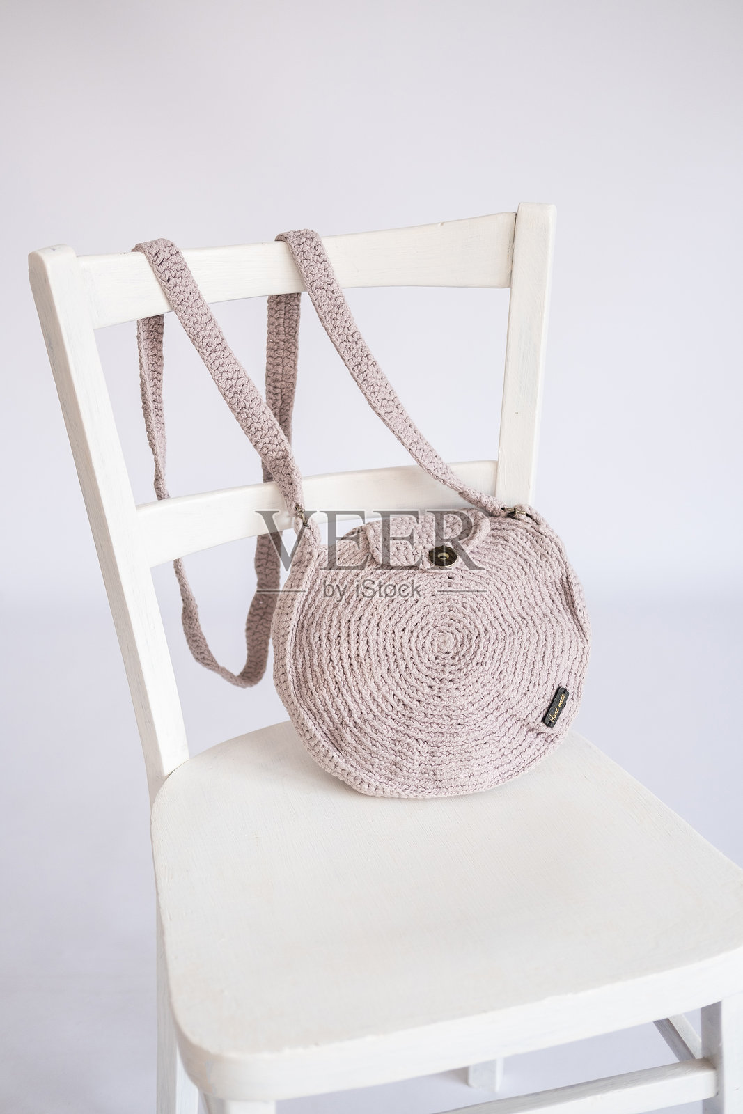 手工粉色钩针包，标签上有“手工制作”的无品牌文字，放在简约白色椅子上照片摄影图片