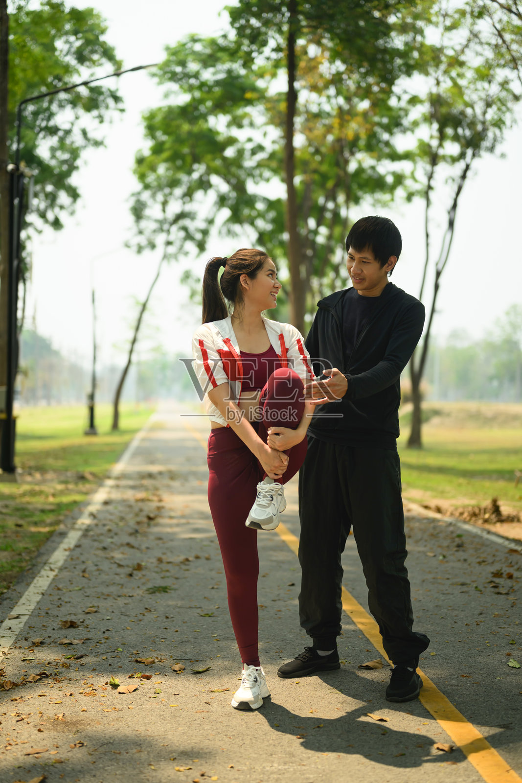 年轻男子在宁静的小路上帮助他的伴侣拉伸，为跑步或锻炼做准备。健康生活方式概念照片摄影图片