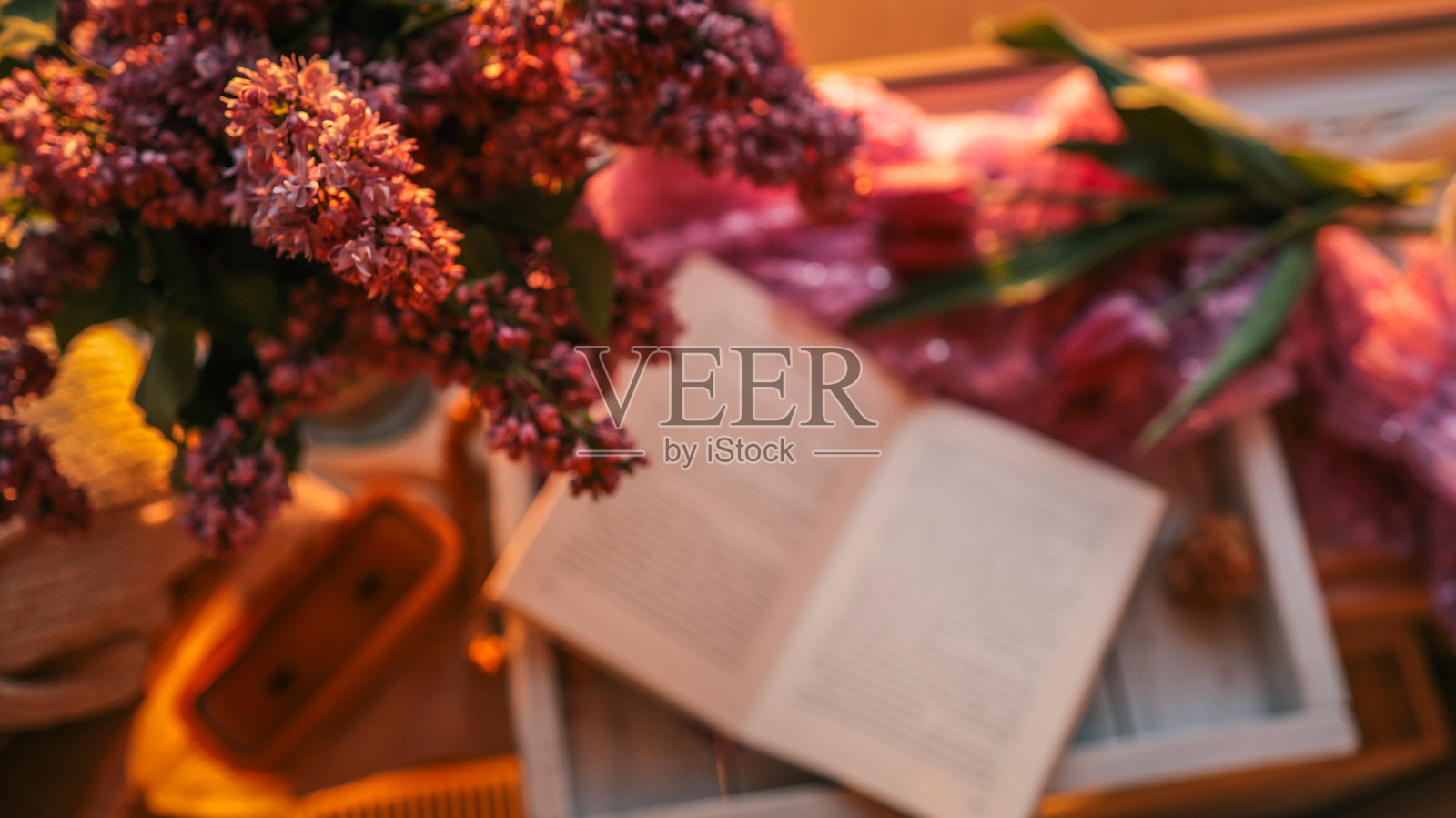 窗边的托盘上放着一束紫丁香和一本打开的书，温暖的夕阳光线洒下，柔和的焦点和浪漫的氛围，唤起一个宁静的春夜，充满平静与灵感。照片摄影图片