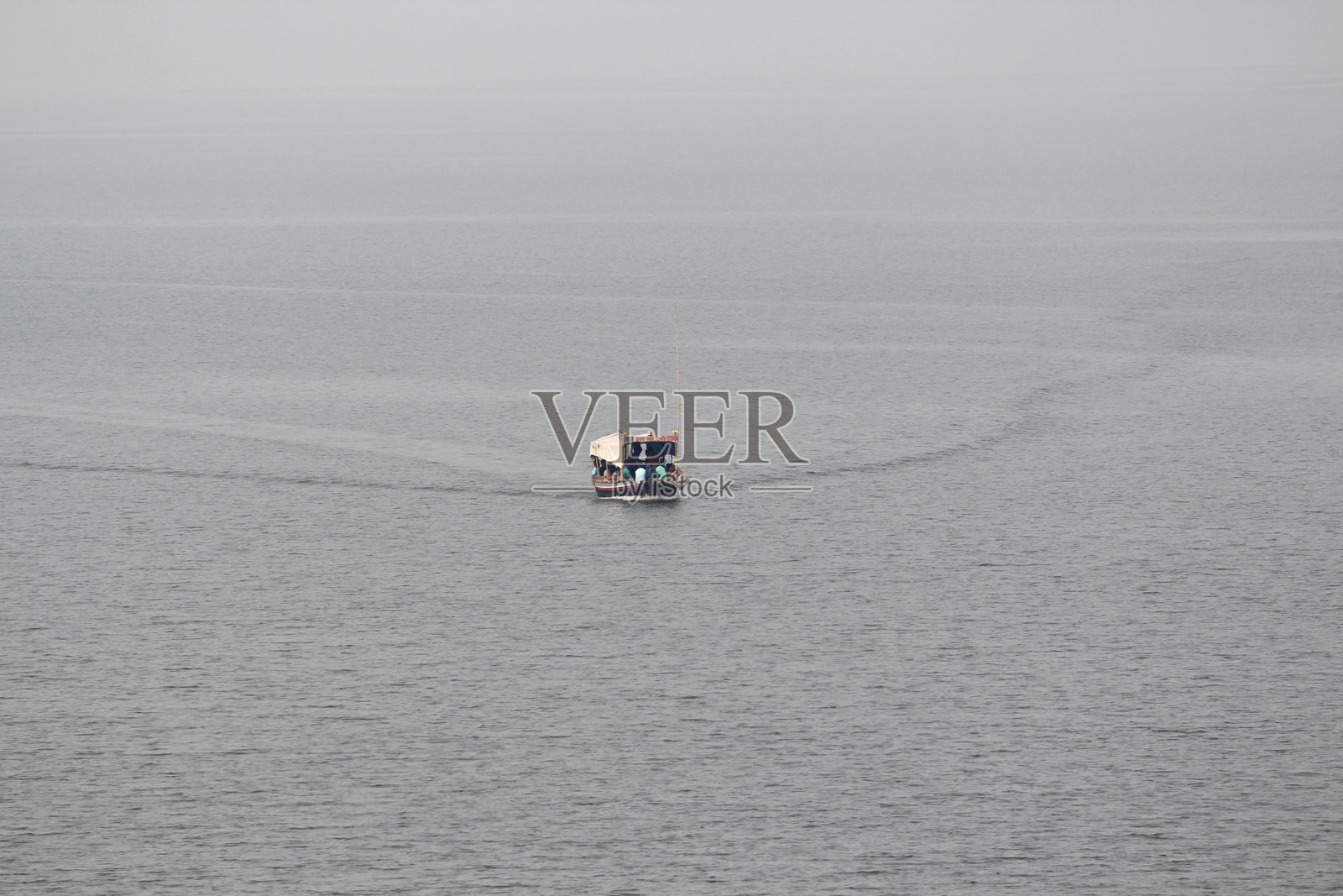 一艘载着许多乘客的船静静地漂浮在平静的湖中央。水面平静，气氛宁静而安详。照片摄影图片