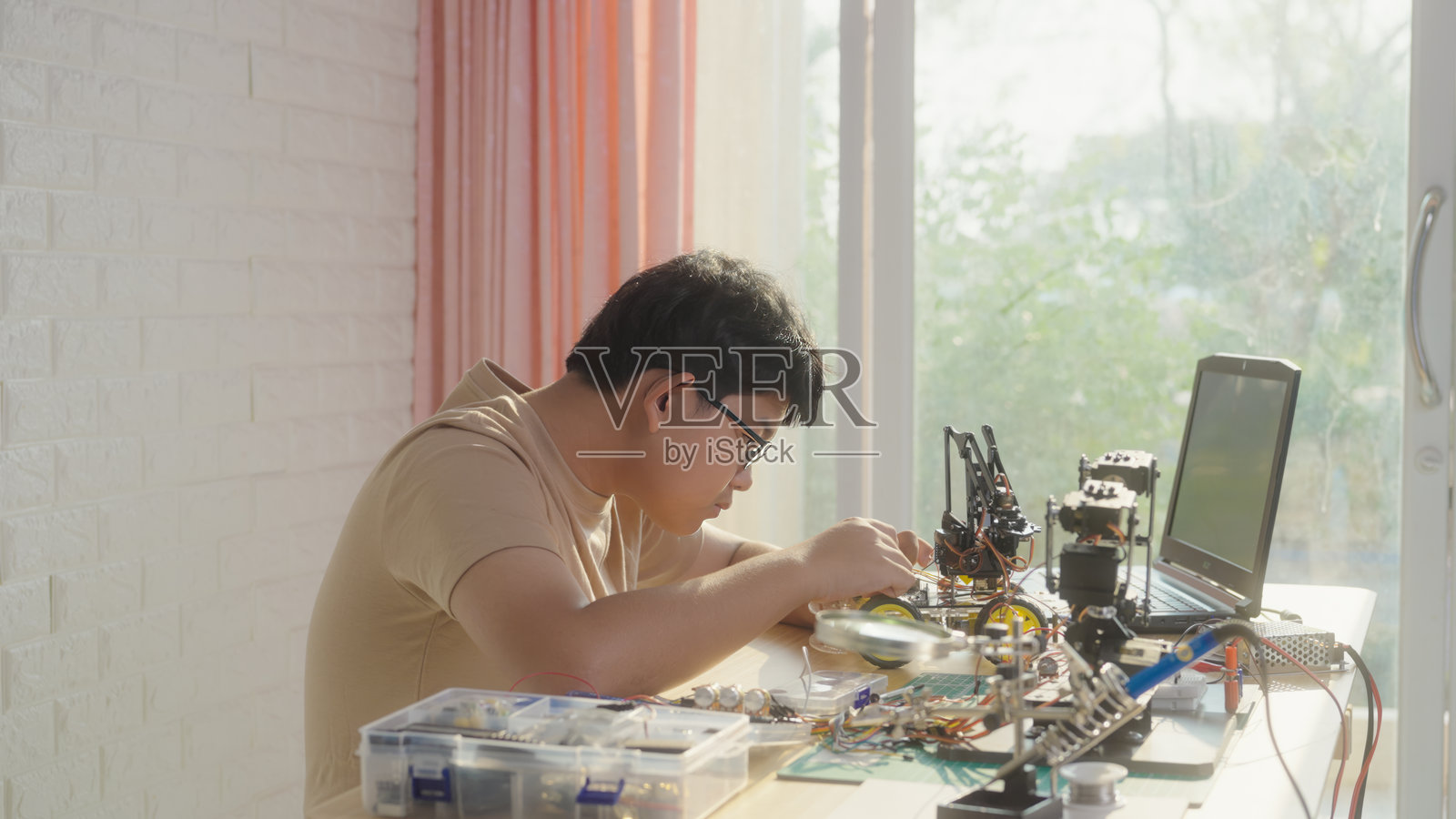 亚洲少年正在用笔记本电脑和工具制作机器人汽车照片摄影图片