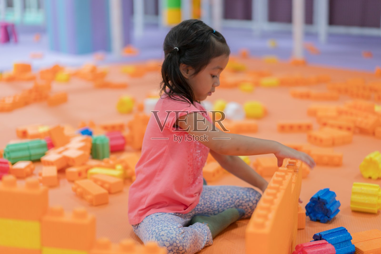 一个年轻女孩专注于用大型轻质泡沫块搭建塔楼。她快乐的表情反映了与这些安全且富有趣味的玩具一起玩耍的乐趣和创造力。照片摄影图片