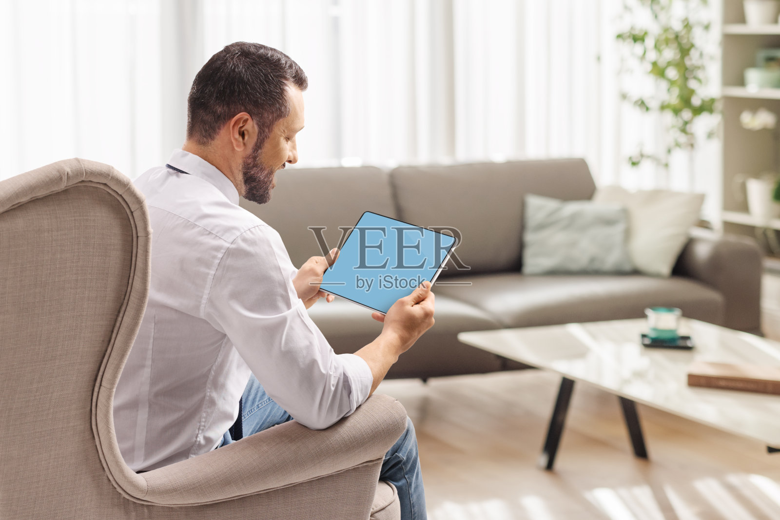 男人坐在家里的扶手椅上使用平板电脑照片摄影图片