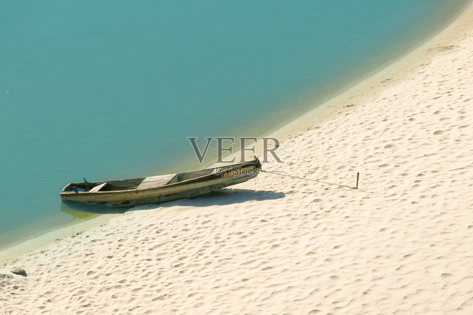 静谧的沙滩上搁浅的木船，旁边是平静的蓝色海水照片摄影图片