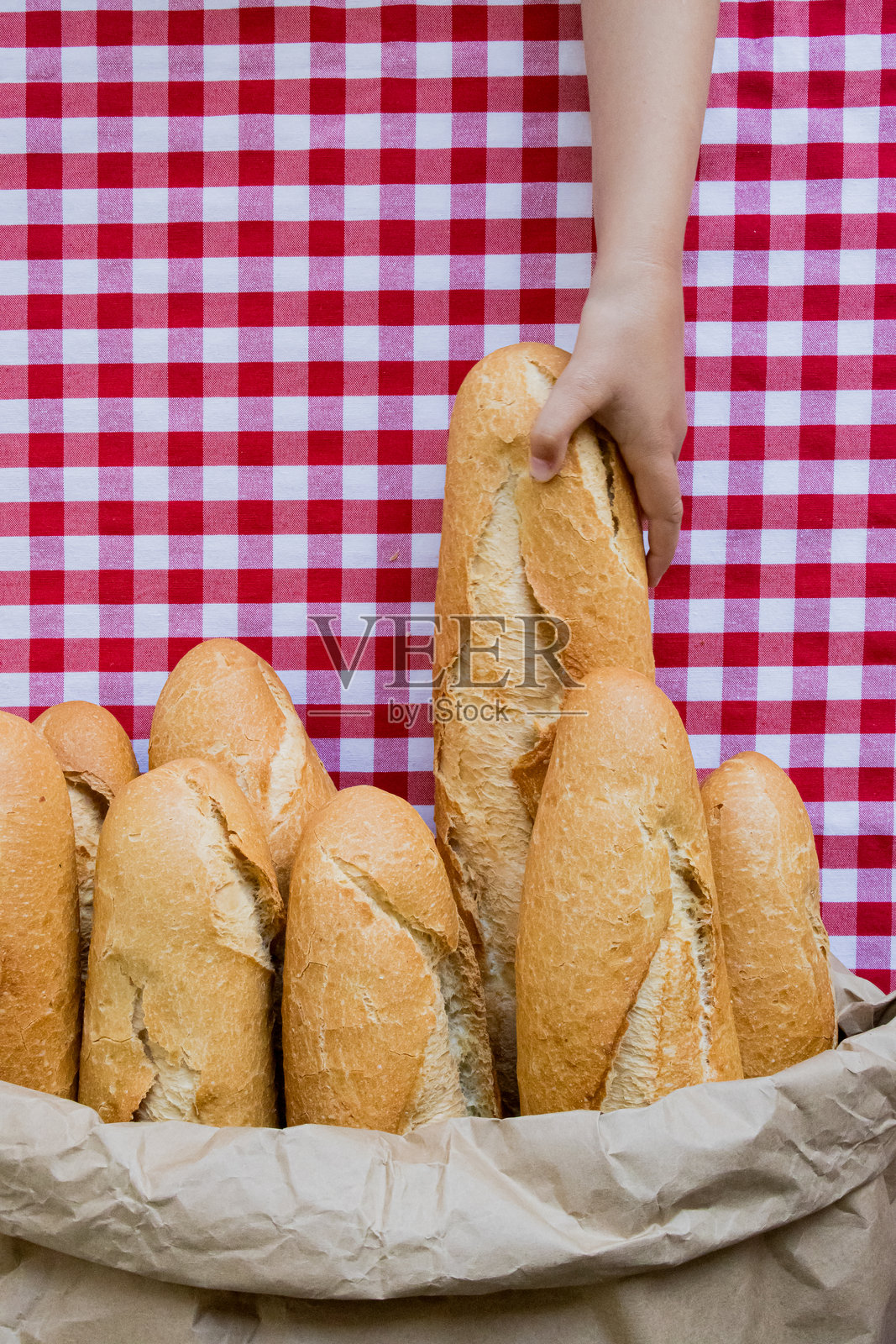 女性手在红色格子桌布上挑选法式面包照片摄影图片