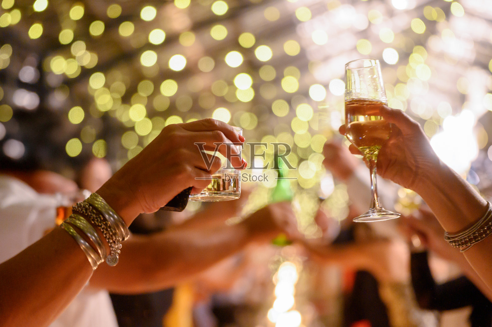节日庆祝活动，手举饮品，背景是金色灯串的虚化效果照片摄影图片