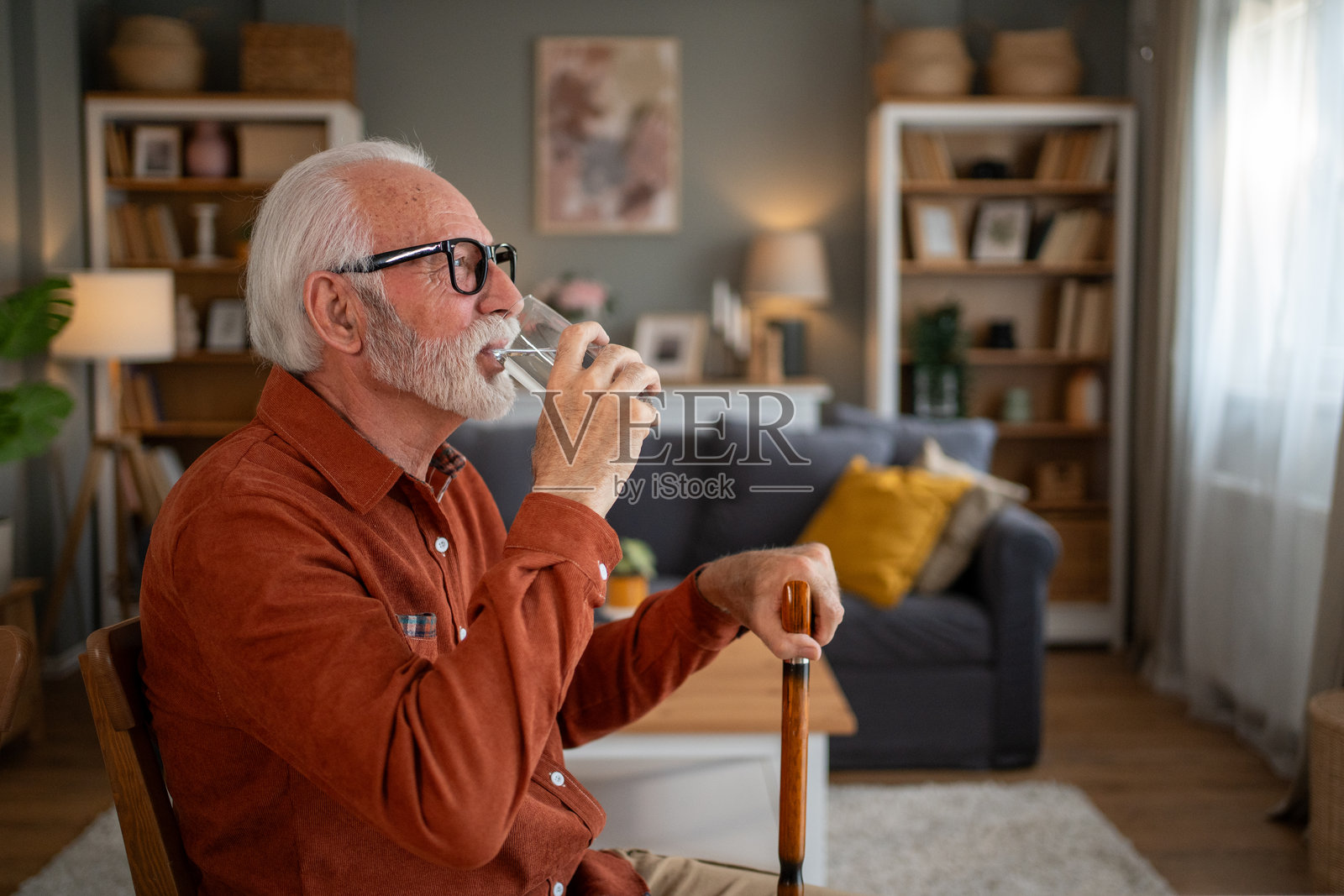 老年男子在家中喝水并握着拐杖照片摄影图片