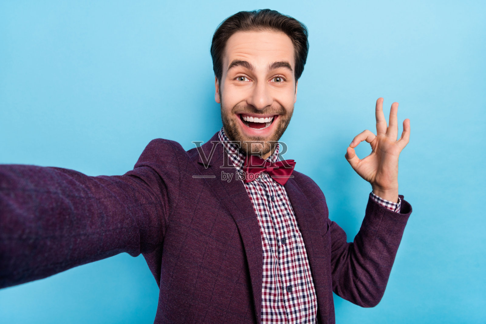 年轻帅气的男人开心地自拍，做出“OK”手势，背景为蓝色。照片摄影图片