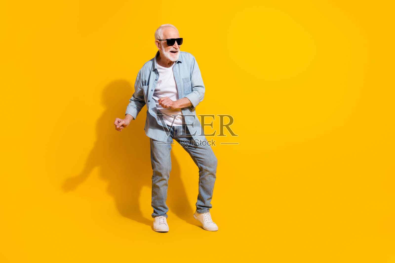 全身照，迷人、快乐、时尚的灰发男士在鲜艳的黄色背景下跳舞。照片摄影图片
