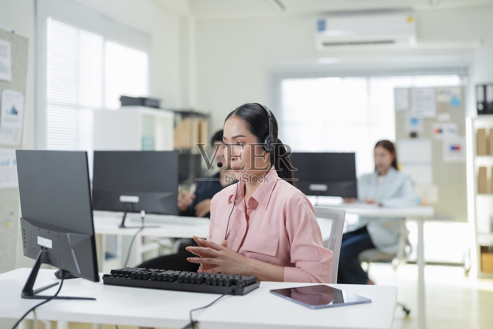 吸引人的年轻女商人在办公室独自坐着，佩戴耳机的特写镜头。电话营销员，电脑和麦克风在帮助台，进行咨询或听取技术支持。照片摄影图片