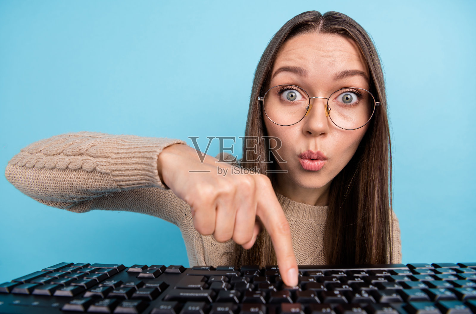 迷人时尚的女孩在明亮的蓝色背景下，惊讶地打字、发信息、聊天，撅嘴按按钮。照片摄影图片