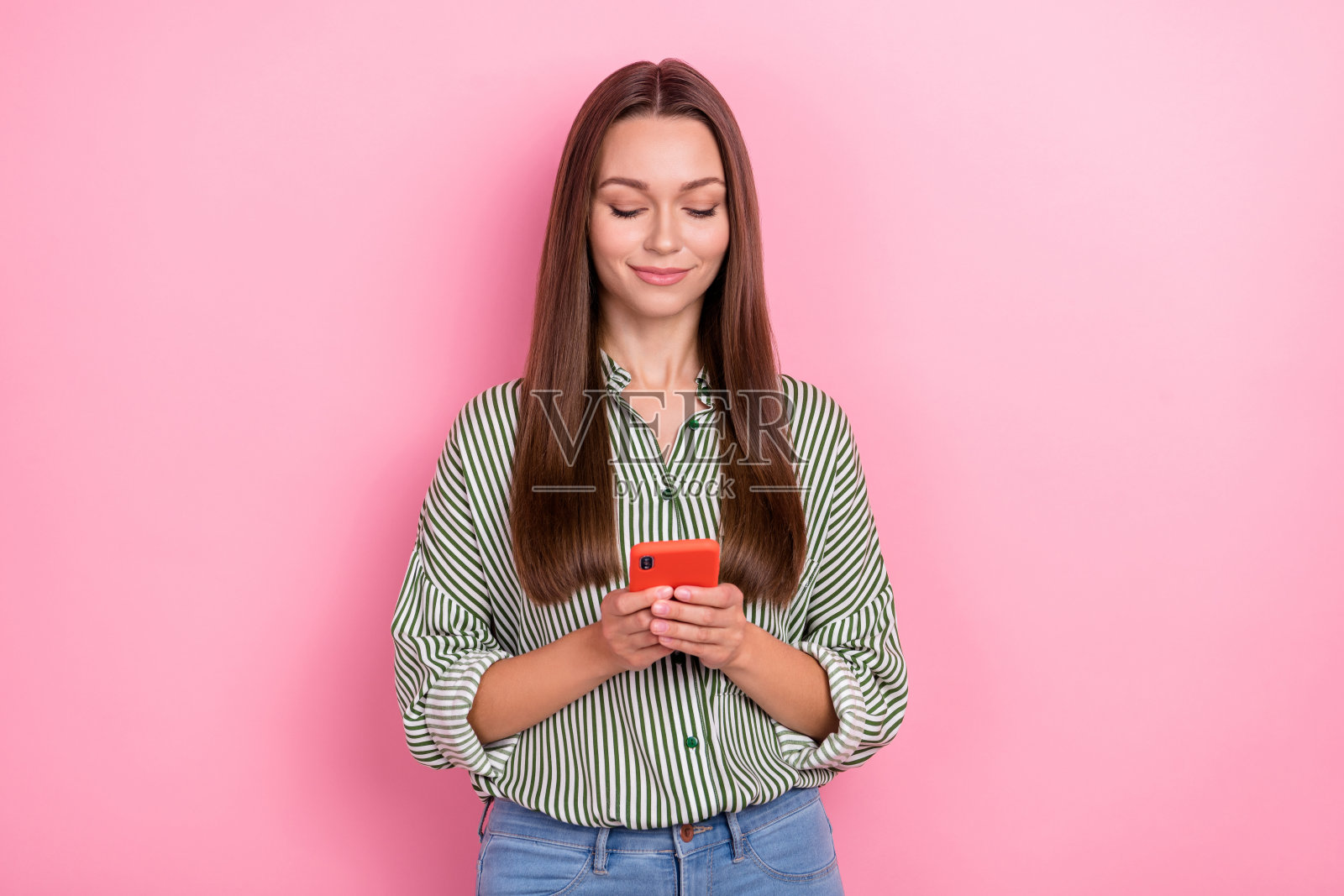 迷人漂亮的女人穿着条纹衬衫，手持现代设备，背景为粉色。照片摄影图片