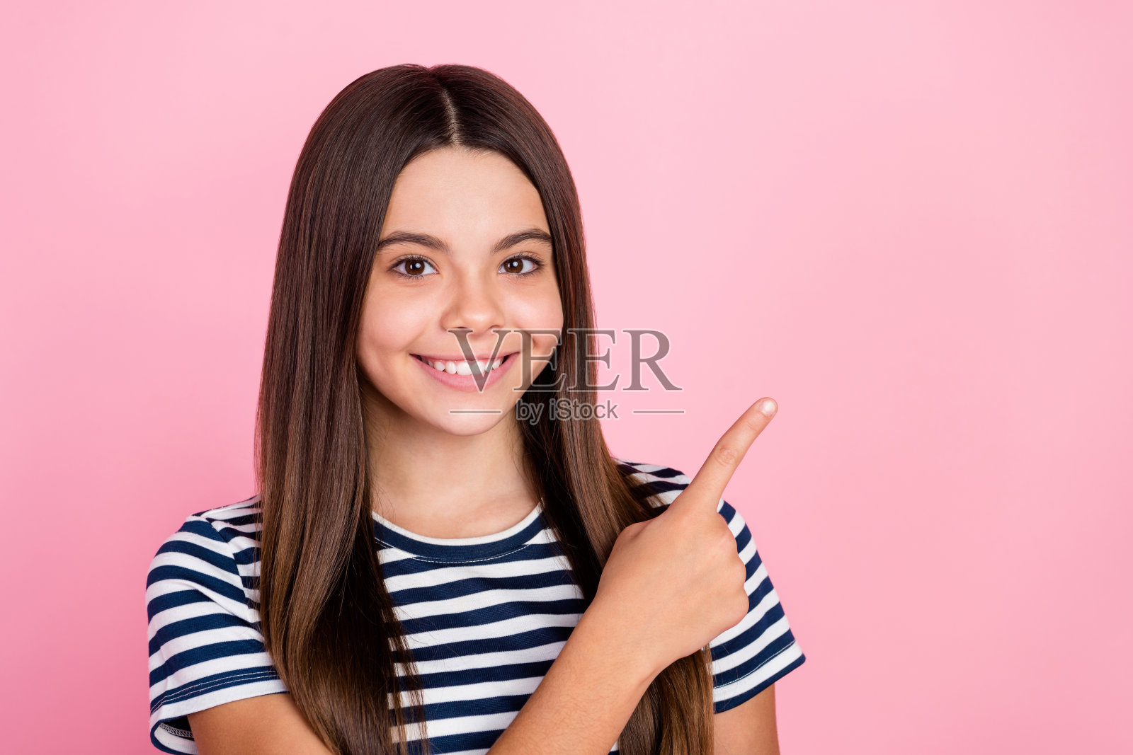 穿着条纹衣服的可爱女孩指着空白处，背景为粉色。照片摄影图片