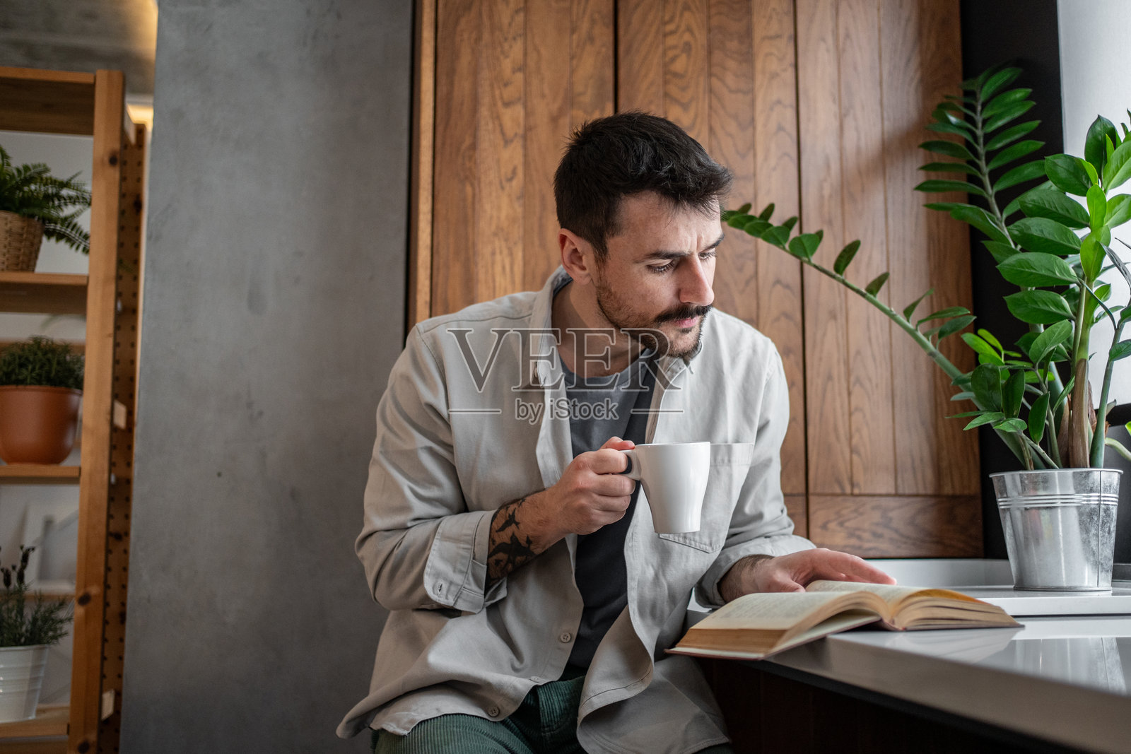 年轻男子在现代厨房中享受咖啡和书籍照片摄影图片