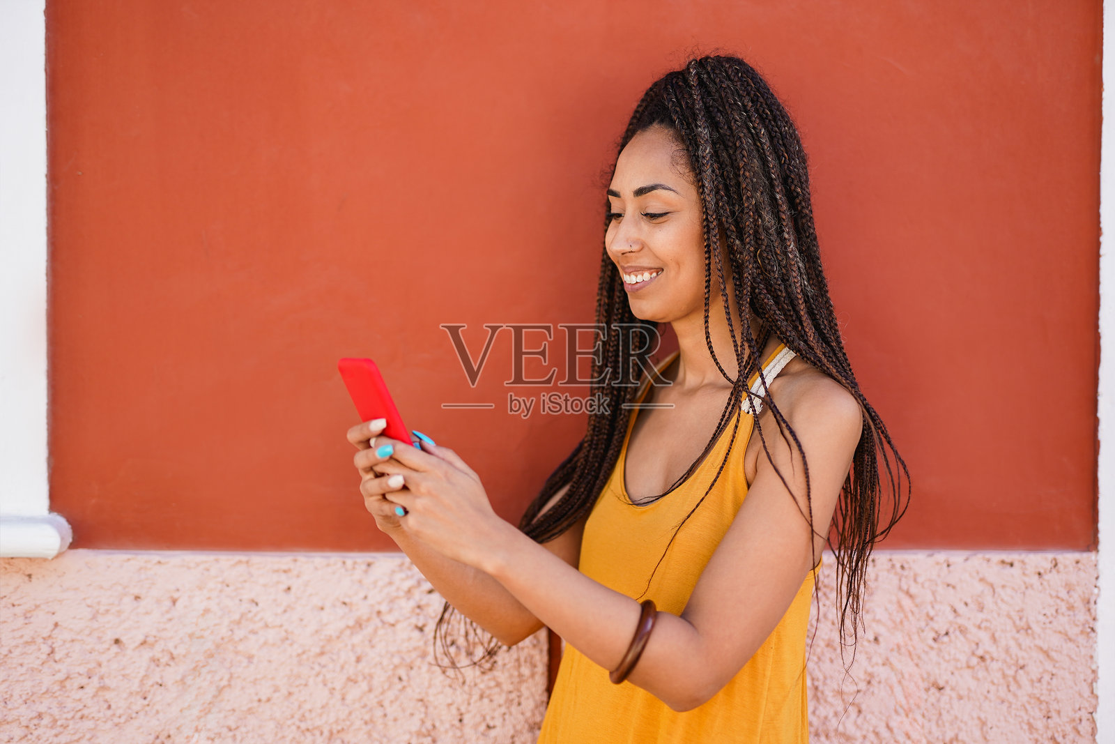 快乐的年轻拉丁裔女性在夏季的房子外使用手机 - 女孩、社交媒体和科技概念照片摄影图片