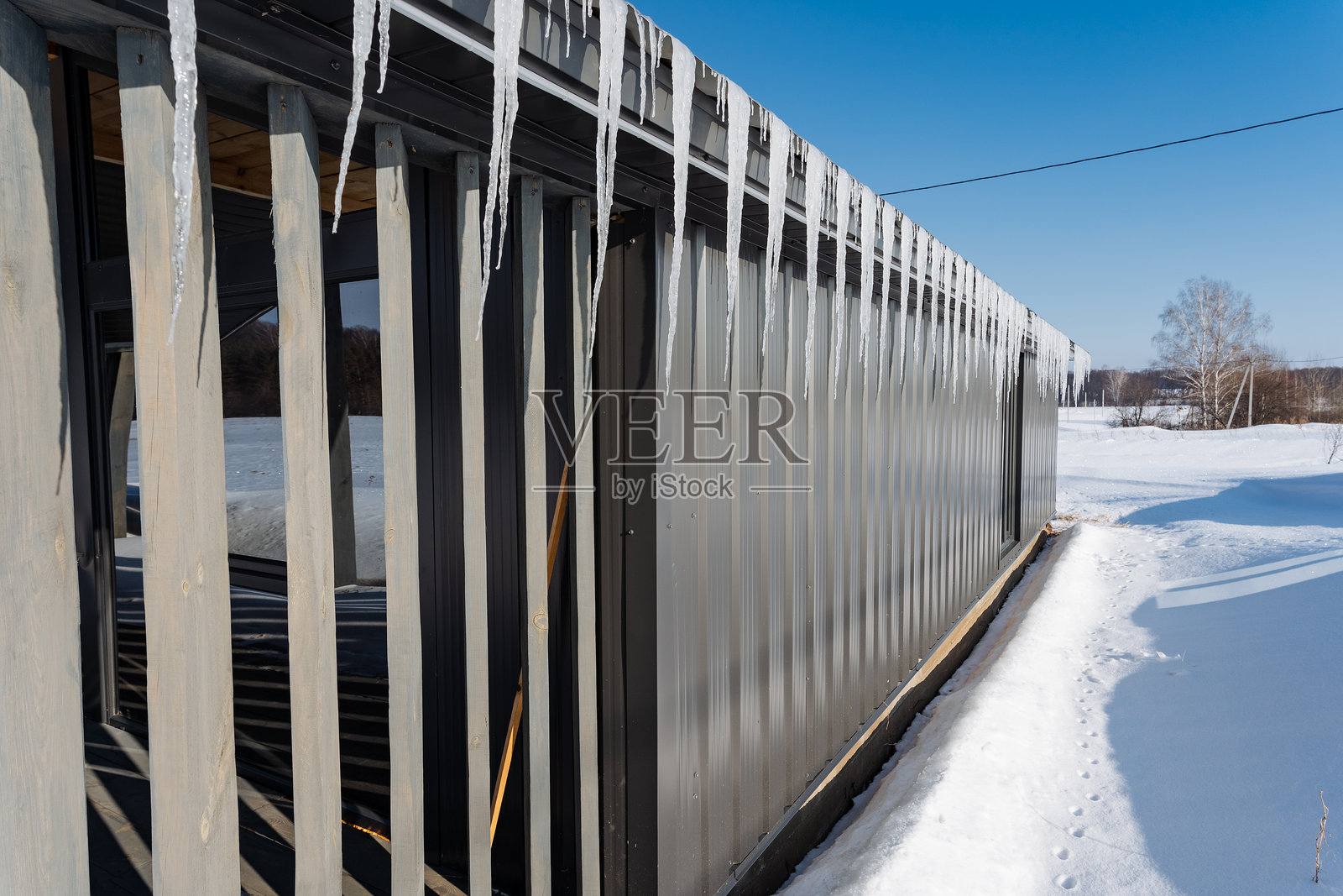 冰柱优雅地悬挂在一座完全被蓬松白雪覆盖的高楼边缘，形成了一个令人惊叹的冬季景观，供每个人欣赏和享受。照片摄影图片