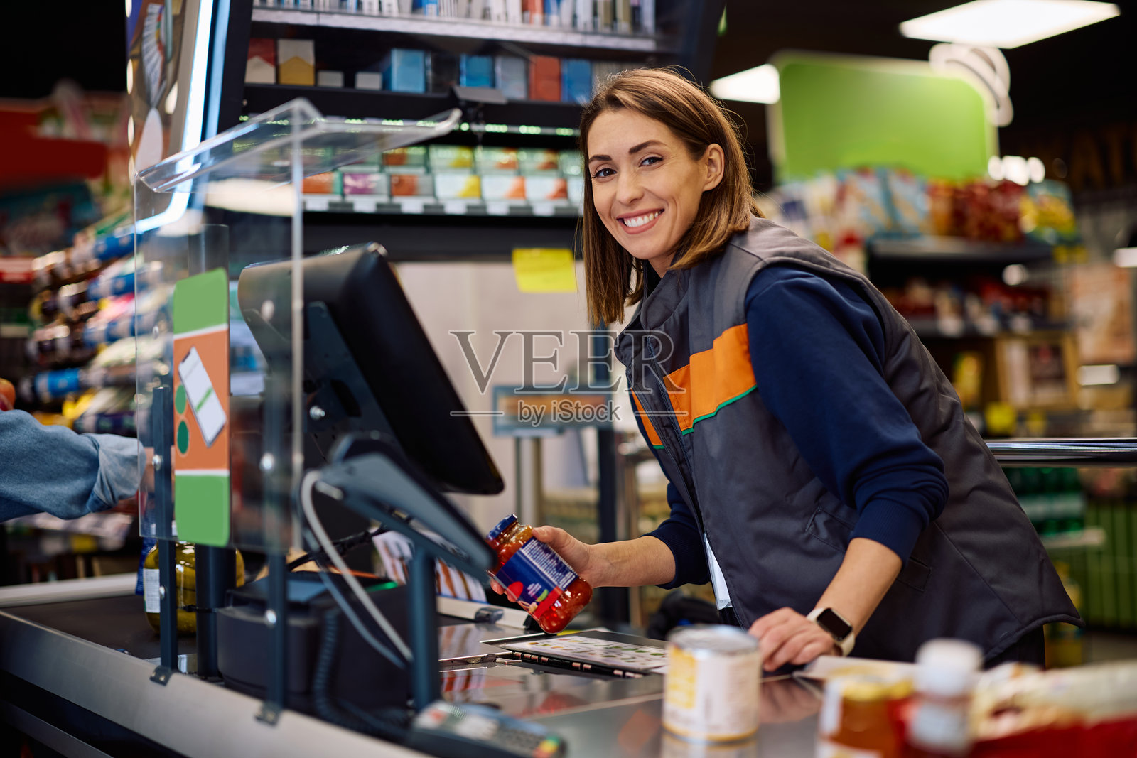 快乐的收银员在超市结账时扫描商品并看向镜头。照片摄影图片