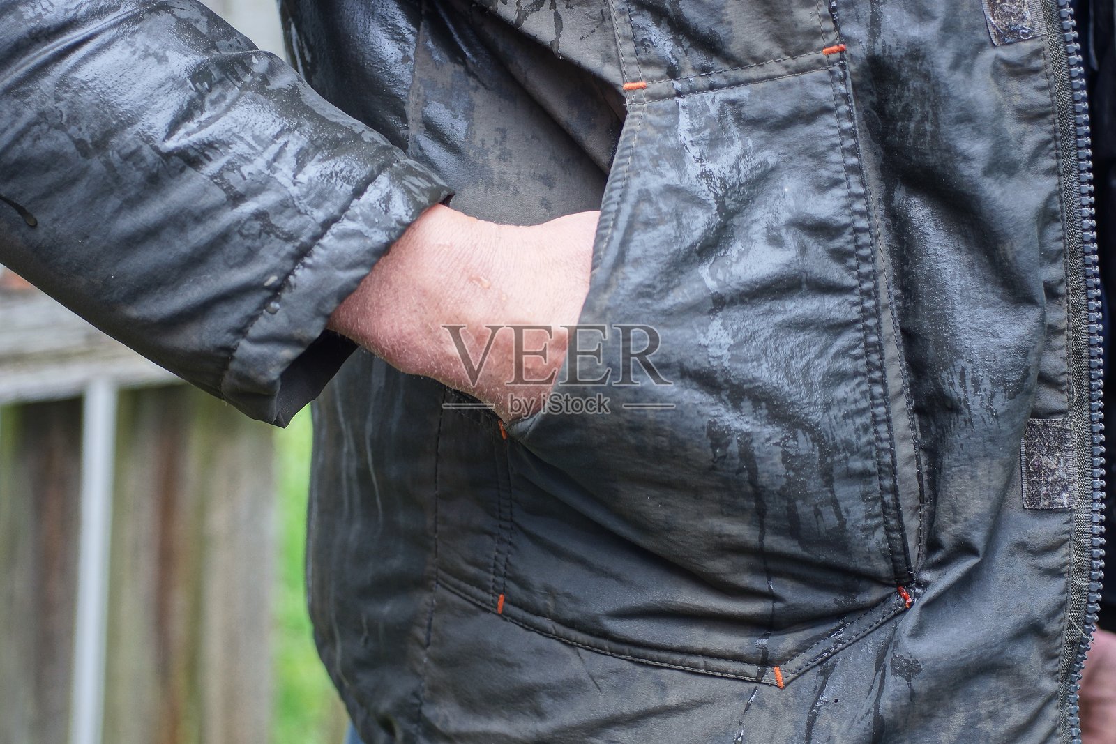 一名男子穿着灰绿色湿漉漉的夹克，手插在口袋里。照片摄影图片