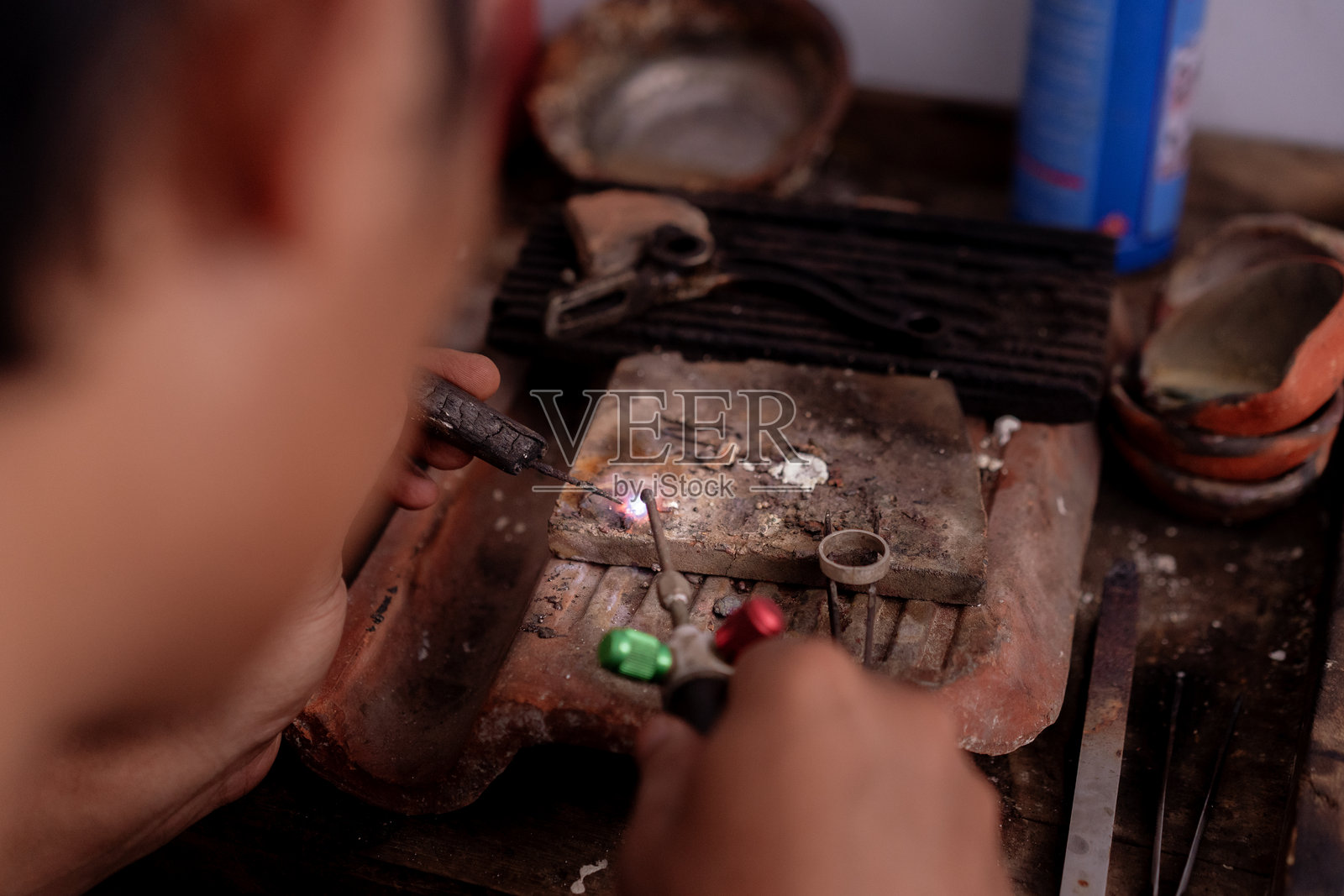 特写镜头：男子手持火焰喷枪焊接和熔合银戒指照片摄影图片